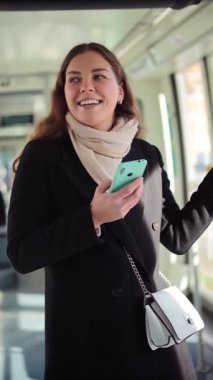 Neşeli bir kadın, bir toplu taşıma aracında dururken akıllı telefonuna odaklanır. Yolcu olarak geçirdiği zamanın tadını çıkarır ve mobil cihazıyla çeşitli uygulamaları inceler.