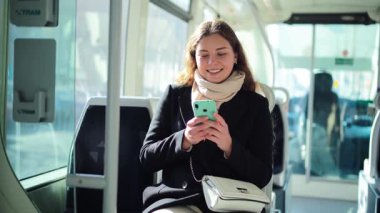 Toplu taşıma araçlarında otururken akıllı telefonuyla meşgul olan neşeli bir kadın, internette gezinirken açıkça eğleniyor ve her gün işe gidip gelirken arkadaşlarıyla bağlantıda kalıyor.