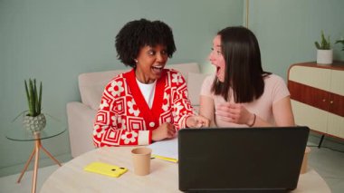 Bir çift neşeli arkadaş, bir dizüstü bilgisayarla etkileşime girerken keyif ve heyecan dolu bir anı paylaşıyorlar, önemli bir başarıyı kutluyorlar ve gerçek mutluluklarını gösteriyorlar.