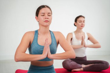 Yoga meditasyonuna kendini adamış iki kadın, elleri dua jestine hazırlanmış, huzur ve farkındalığı somutlaştırarak, sağlık yolculukları sırasında iç huzur ve ruhsal dengeyi arıyorlar.