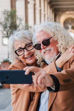 Mutlu son sınıf çifti cep telefonlarıyla selfie çekerken neşeli ifadeleri ve şefkatli kucaklamalarıyla sevgi ve neşe saçarak unutulmaz bir anı yakalıyorlar.