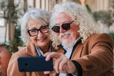 Mutlu son sınıf çifti cep telefonuyla selfie çekerken mutlu anlarını yakalarken birbirlerine gülümseyip şefkat gösteriyorlar. Hayatı ve aşkı bir arada kutluyorlar.