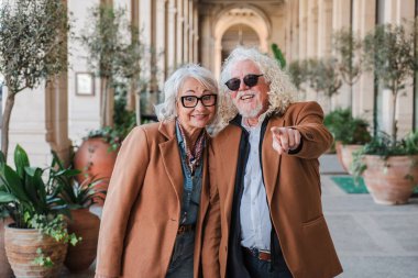 Sevinçli yaşlı çift neşeli bir etkileşim içinde, büyüleyici bir görüntüye işaret ederek, birlikte keyifli bir gezinti yaparken ve eğlenirken neşe ve arkadaşlıkla dolu