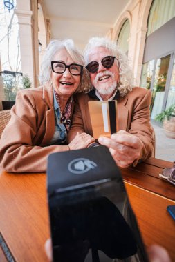 Birlikte keyifli bir yemek yerken kredi kartlarını hevesle gösteren neşeli yaşlı bir çift, paylaşılan anlarını ve günlük alışverişlerinde buldukları mutluluğu gözler önüne seriyor.