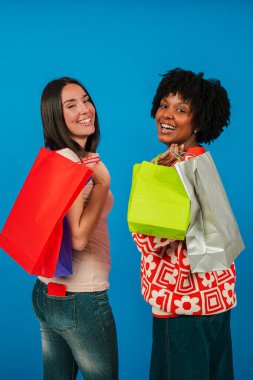 A lively image of two cheerful women engaging in a fun shopping adventure, enthusiastically displaying colorful shopping bags, embodying the joy of friendship and the excitement of retail therapy.