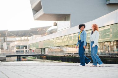 Two cheerful women strolling side by side, sharing laughter and enjoying their time together while exploring the area with a sense of connection and joy, creating unforgettable memories.