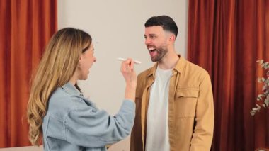 Happy couple embracing each other while joyfully revealing a positive pregnancy test result, radiating love and excitement in a cozy indoor setting with warm lighting and soft colors.