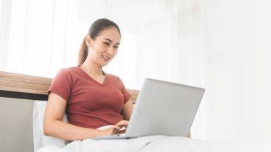 İnternet teknolojisi konseptiyle yaşam tarzı rutini. Genç Asyalı kadın teletıp zihinsel sağlığı için dizüstü bilgisayar kullanıyor ya da internetten alışveriş yapıyor. İnsanlar yatak odasında dinleniyor..