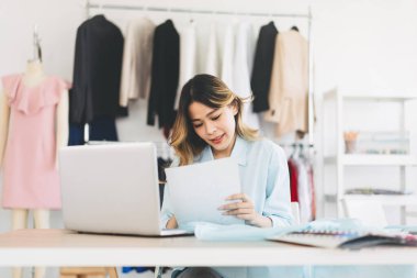 People working in fashion design concept. Young adult asian woman designer using laptop computer for internet online marketing contact customer or sale engagement. Workshop studio background.