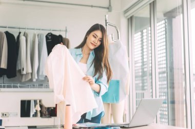 People tailor working in fashion design concept. Young adult asian woman designer using laptop computer for internet online marketing with customer for sale engagement. Workshop studio background.