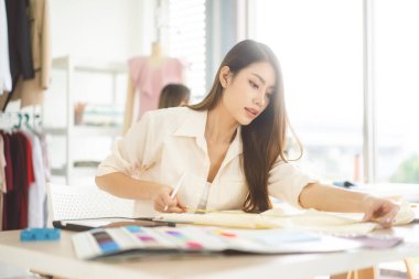 People tailor working in fashion design concept. Young adult asian woman designer sit and making clothes for business at start up studio dressmaker.