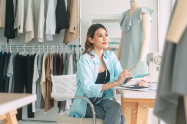People tailor work or study in fashion design studio concept. Young adult asian woman designer busy making clothes. Background with sewing machine and mannequin.