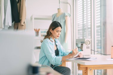 People tailor work or study in fashion design studio concept. Young adult asian woman designer busy making clothes. Background with sewing machine and mannequin.