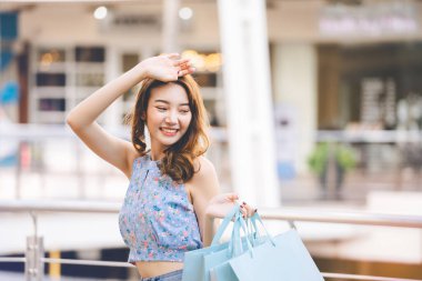 Wellbeing single lifestyle on holidays. Happy young adult southeast asian woman with shopping bags on day. Wear blue shirt with long hair.