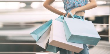 People spending money shopaholic concept. Front of adult asian woman with shopping bags in blue theme. Weekend city people buying lifestyle. Banner size background.