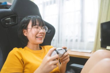 Happy smile nerd young adult asian gamer woman wear eyeglasses play a online game. People leisure lifestyle at home.
