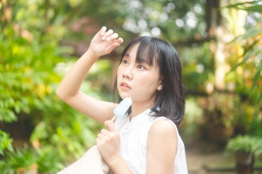 Portrait happy asian teenager woman on summer season. Relax eating ice cream at home outdoor garden. Girl wear white dress shirt.
