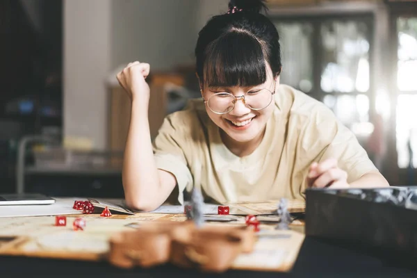 Role playing tabletop and board game hobby concept. Happy young adult asian woman enjoying with storytelling fantasy adventure. Blur foreground with monster miniatures and dice component.