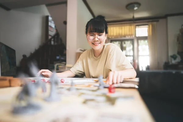 Role playing tabletop and board game hobby concept. Happy young adult asian woman enjoying with storytelling fantasy adventure. Blur foreground with monster miniatures and dice component.