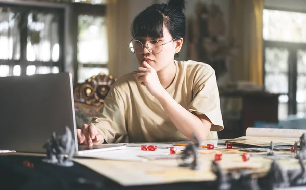 Role playing tabletop and board game hobby concept. Young adult asian woman enjoying with storytelling. Blur foreground with monster miniatures and dice component.