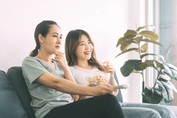 Two young adult woman living together with relationship concept. Southeast asian people couple relax lifestyle on sofa eating popcorn life moments at home or apartment.