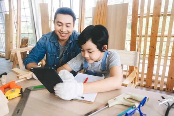 Southeast asian family father and son diy activity together at home concept. Dad teach education child via digital tablet technology using tools about carpenter skill workshop. Workbeach with tools