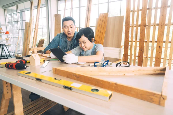 Southeast asian family father and son diy activity together at home concept. Dad teach education child via digital tablet technology using tools about carpenter skill workshop. Workbeach with tools