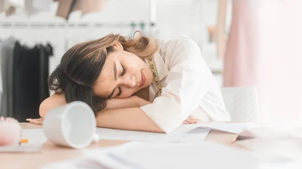 People tailor working in fashion design concept. Young adult asian designer woman tried and sleeping at workshop table. Background in business start up studio dressmaker.