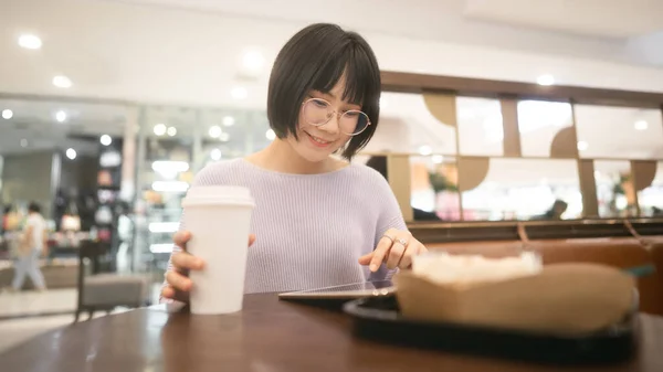 Young adult business asian woman with modern gadget technology. Using tablet for online internet at indoor public cafe on day. Single people lifestyle in city concept.