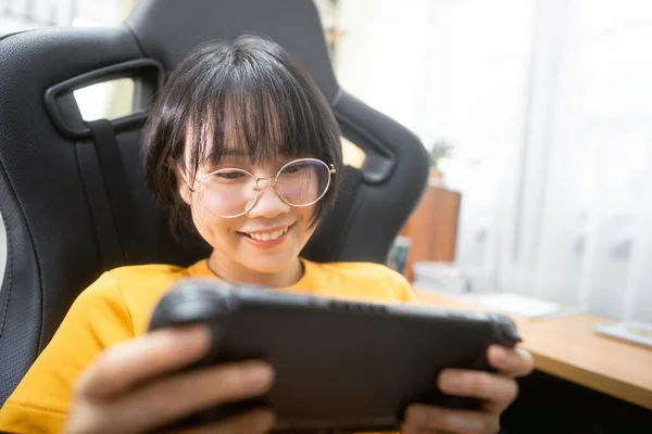 Nerd style happy smile young adult asian gamer woman wear eyeglasses play a online game. Competition for victory mood. People leisure lifestyle at home.