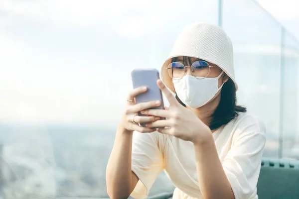 Young adult asian female wear face mask for protect virus corona or covid 19. Using mobile phone for online technology outdoor lifestyle at public place.