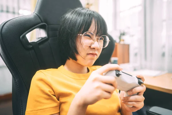 Nerd style young adult asian gamer woman wear eyeglasses play a online game. Competition for victory mood. People leisure lifestyle at home.