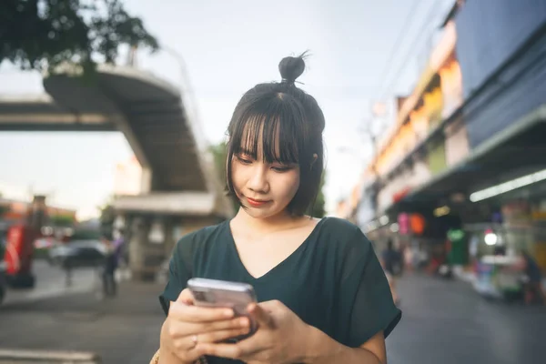 快乐地笑着年轻的亚洲女人晚上在户外街道市场 在网上使用手机申请日期 休闲时尚的生活方式 — 图库照片