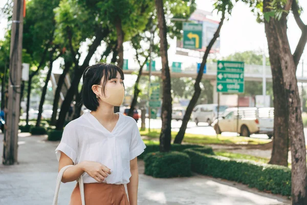 年轻的成年亚洲职业女性戴着口罩 以保护病毒电晕或眼镜蛇 防止空气污染 日光浴时 在有自然环境的街道附近的人行道上行走 — 图库照片