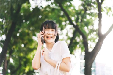 Young adult southeast asian business single woman using smartphone talking with friend. Happy face and laugh. City break lifestyle working people. Backgroud at outdside on day.