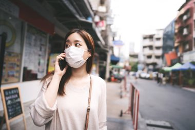 Casual business young asian single woman wear mask for new normal lifestyle in city. Talking by smartphone on sidewalk street outdoor area on day. Bangkok, Thailand.