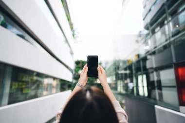 Rear view of asian woman holding smart phone. People city network connect with internet concept. Indoor urban building on day background.
