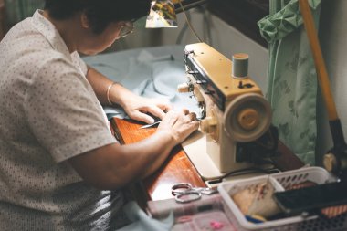 Retriement tailor southeast asian elderly crafting a cloth by sewing machine. Baby boomer generation mature working at home concept. Life moments in candid portrait authentic people.