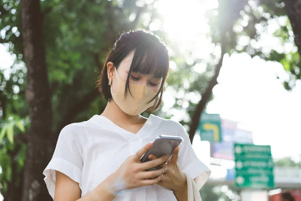 年轻的成年亚洲职业女性戴着口罩 以保护自己免受病毒的侵袭或感染 使用手机应用程序 城市人每天接种疫苗后的生活方式 — 图库照片