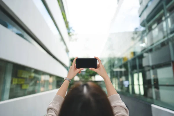Shoulder view of woman holding mobile phone empty screen with blur city background on day.