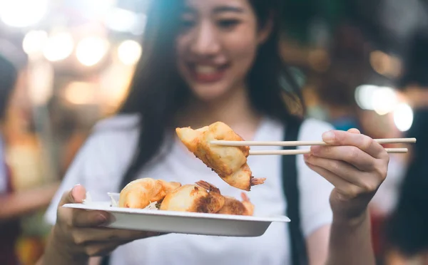 Poeple travel and eating street food concept. Closeup gyoza dish holding by happy asian woman at Chinatown Yaowarat market, Bangkok, Thailand.