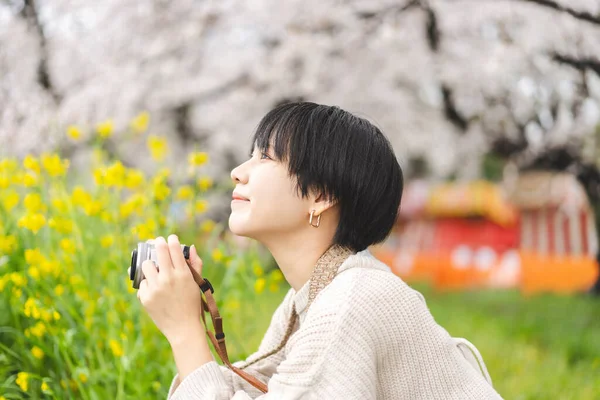 桜の木を見て若い大人の日本人観光客の女性のサイドビューの肖像画 カメラで旅のライフスタイル 4月の日本の花見祭り — ストック写真