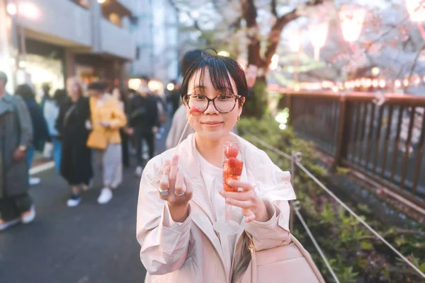 日本東京シティ中目黒桜祭りの有名な目的地 若い大人のアジアの女性がイチゴのスパークリングワインを食べる 夜の街観光での日本人の生活 — ストック写真