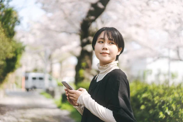 スマートフォンを使ってアジア系の若い女性 オンラインのための入力日付アプリやソーシャルメディア 春の屋外公園での日本人のライフスタイル コピースペースの背景 — ストック写真
