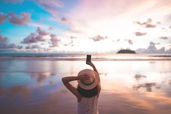 Genç, yetişkin, Asyalı bir turistin kumsalda yürüyüp fotoğraf çekmek için akıllı telefon kullanmasının arka görüntüsü. Güneydoğu Asya ve Man Okyanusu 'nda yurt içi seyahatler. Phuket, Tayland.