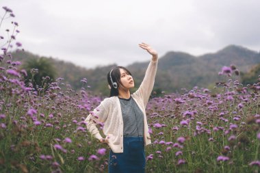 Doğa konseptinde doğa seyahati. Asyalı genç bir kadının portresi çiçek tarlasında rahatlıyor. Kulaklıkla müzik dinlemek ve keyfi yerinde dans etmek..