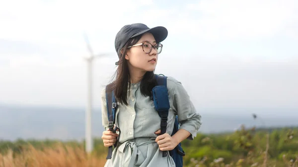 青いバックパックで若い大人のアジアの旅行者の女性側のビュー 自然の屋外で眼鏡や帽子を着用立っている 夏休みの一人旅のコンセプト — ストック写真