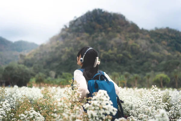 Outdoor travel in nature concept. Top of mountain rear view young adult asian woman backpack traveler in flower blossom park field on spring or summer.