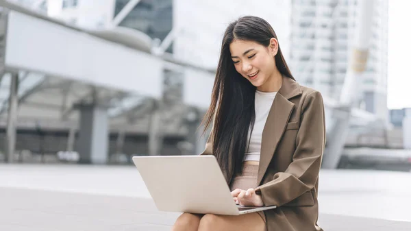 工作时使用笔记本电脑的亚洲年轻女性自由职业 美丽的微笑面对长发 白天坐在室外 采用现代技术的城市居民生活方式 — 图库照片