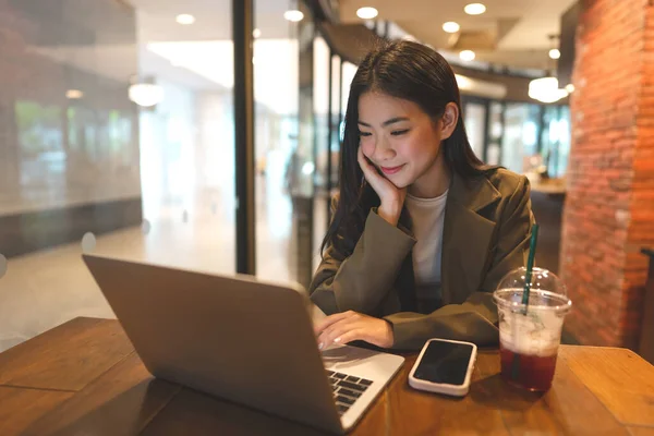 在咖啡店使用笔记本电脑工作的亚洲年轻女性自由职业 城市人的生活方式与现代技术日新月异 数字游牧民族 笑容满面 — 图库照片